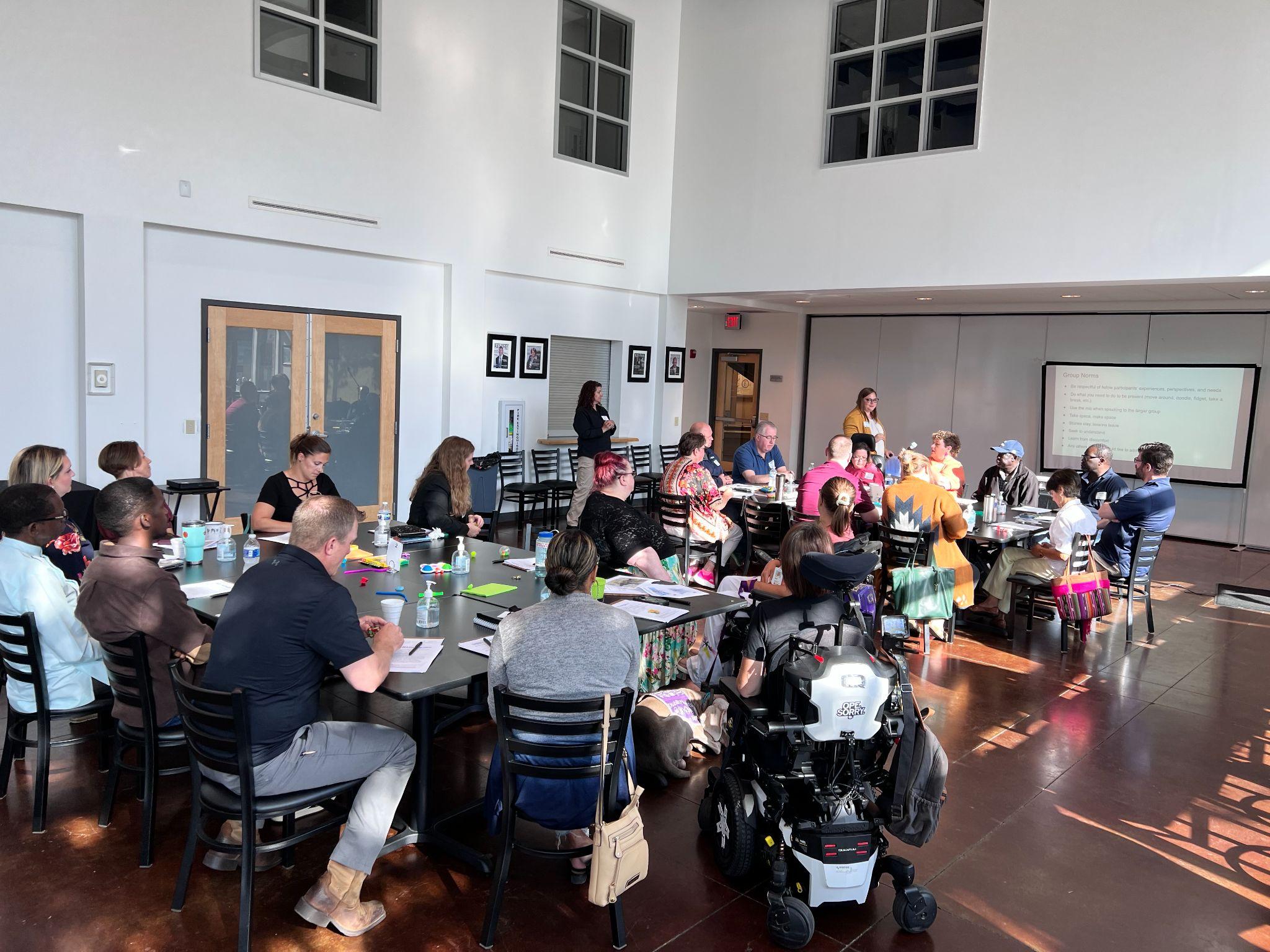 people gathered around tables in a large, sunny room