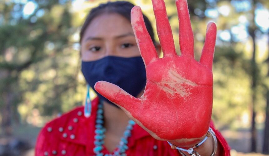 A person with a dark face mask on holding up a hand that is painted red.